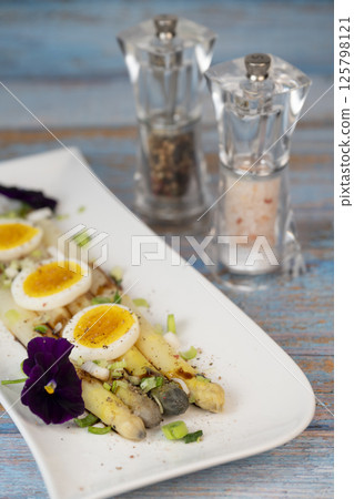 Baked asparagus with boiled egg in big white plate on blue background Baked asparagus with boiled egg in big white plate on blue background 125798121
