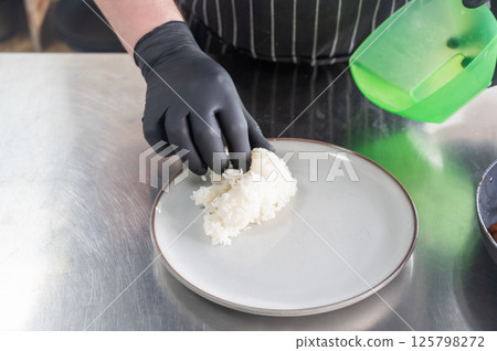 The chef puts boiled rice on a plate.  125798272