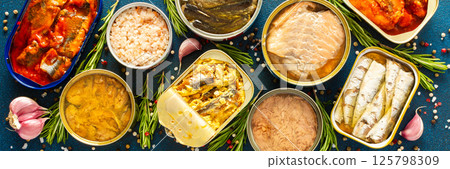 Enjoy an assortment of canned fish including salmon, mackerel, sprat, sardine, tuna, herring, and fish pate, displayed in open tins with spices and herbs on a blue background, banner Enjoy an assortment of canned fish including salmon, mackerel, sprat, sardine, tuna, herring, and fish pate, displayed in open tins with spices and herbs on a blue background, banner 125798309