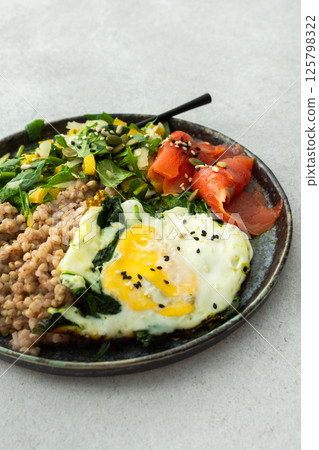 Buckwheat with fried egg and salmon fish, mix salad with fresh herbs and peppers Buckwheat with fried egg and salmon fish, mix salad with fresh herbs and peppers 125798322