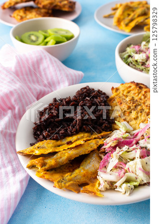 A balanced and nutritious breakfast with brown rice, baked white fish, fresh zucchini-carrot pancakes, a Chinese cabbage salad, and a sweet kiwi dessert, providing a perfect energy boost 125798329