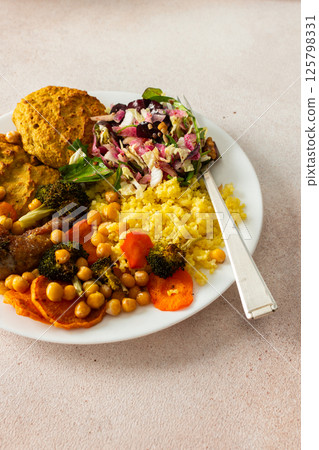 A wholesome breakfast with lentil-zucchini pancakes, millet, roasted chicken neck, sweet potatoes, broccoli, carrots, chickpeas, and a fresh mix salad with radish, nuts, and mung bean sprouts 125798331