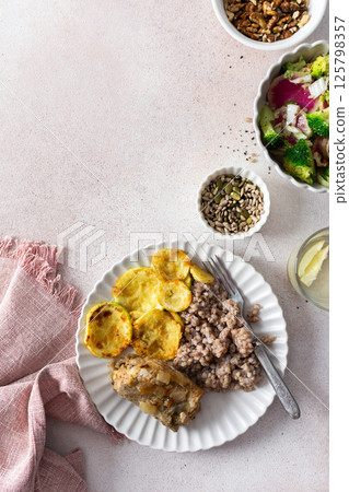 A nutritious, balanced breakfast featuring green buckwheat, fried hake, zucchini, and a fresh broccoli salad with pink radish, seeds, and nuts, offering a wholesome start to the day 125798357