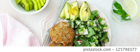 Quinoa cutlets and mixed salad with avocado and radishes, kiwi and water Quinoa cutlets and mixed salad with avocado and radishes, kiwi and water 125798377