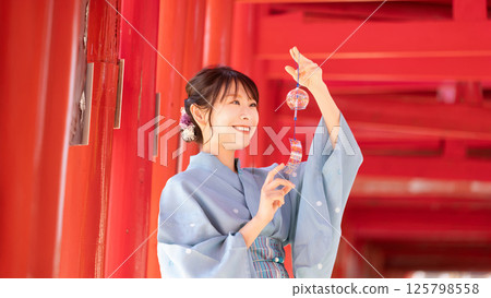 A Japanese woman in a yukata standing at a torii gate holding a wind chime 125798558