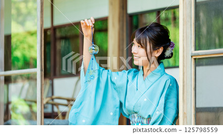 一位身穿浴衣的日本婦女在陽台上拿著風鈴 一位身穿浴衣的日本婦女在陽台上拿著風鈴 125798559