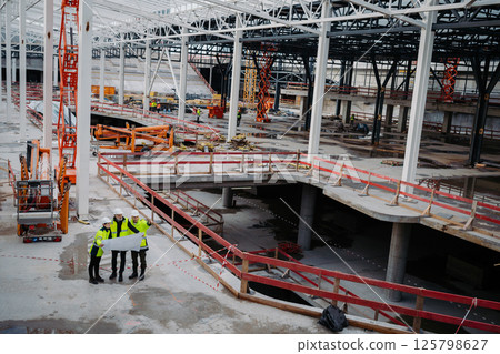 Team of engineers and construction workers reviewing blueprints, building site. 125798627