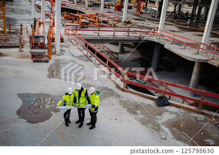 Team of engineers and construction workers reviewing blueprints, building site. 125798630