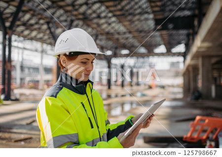 Female engineer checking building documentation on clipboard at construction site. Female engineer checking building documentation on clipboard at construction site. 125798667