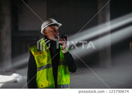 Construction foreman giving instructions over radio during building inspection. 125798674