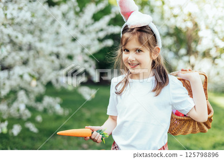 Easter egg hunt. Girl child Wearing Bunny Ears Running To Pick Up Egg In Garden. Easter tradition. Baby with basket full of colorful eggs. 125798896