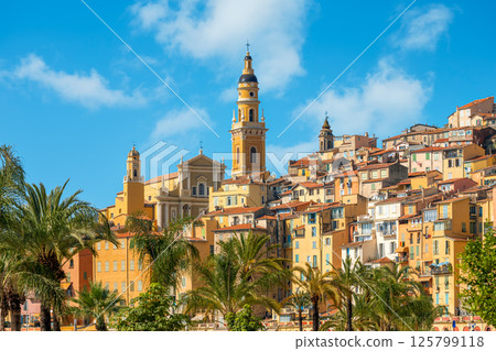 Saint Michel Archange basilica with tall yellow bell tower surrounded by old colorful buildings in Menton, France. 125799118