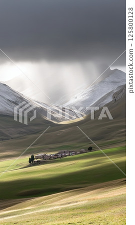 A mountainous landscape with a small village and a storm cloud overhead in the distance 125800128