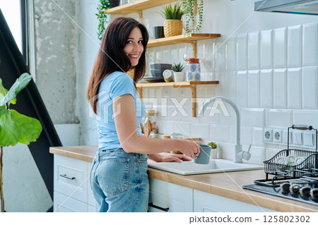 Portrait of beautiful smiling 30s woman with cup in kitchen sink at home 125802302