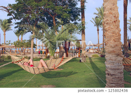 Attractive woman in swimsuit swaying in hammock enjoying summer holidays Attractive woman in swimsuit swaying in hammock enjoying summer holidays 125802436