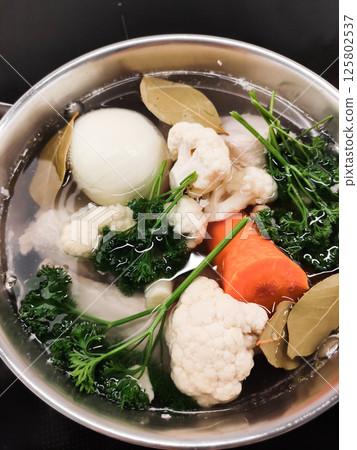 Chef preparing vegetable broth with cauliflower, carrots, onions, and parsley cooking vegetables for making soup 125802537