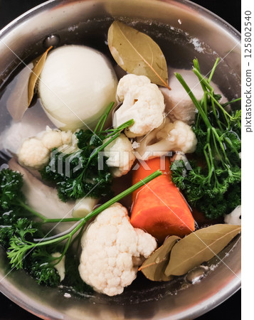 Chef preparing vegetable broth with cauliflower, onion, carrot, parsley and bay leaves cooking vegetables for making soup Chef preparing vegetable broth with cauliflower, onion, carrot, parsley and bay leaves cooking vegetables for making soup 125802540