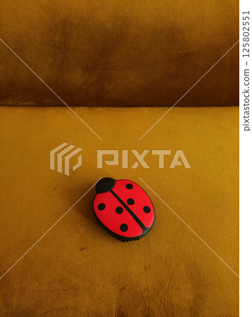Red ladybug pet hair brush for cleaning furniture, car seats, carpets resting on gold velvet sofa copy space 125802551
