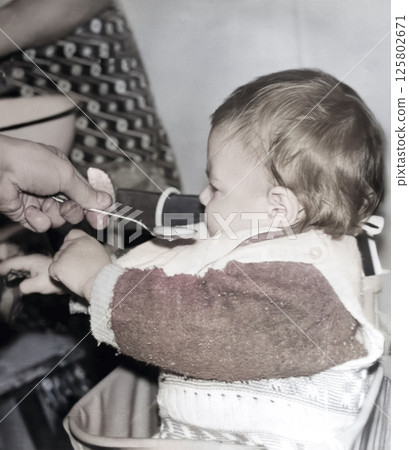 Vintage portrait of a cute little girl being fed porridge with a spoon. Retro photo from 1995. Vintage portrait of a cute little girl being fed porridge with a spoon. Retro photo from 1995. 125802671
