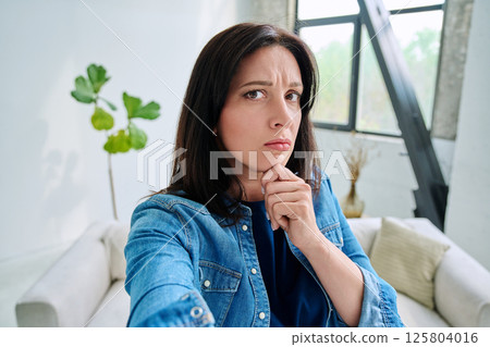 Selfie portrait serious confused beautiful woman in home interior 125804016