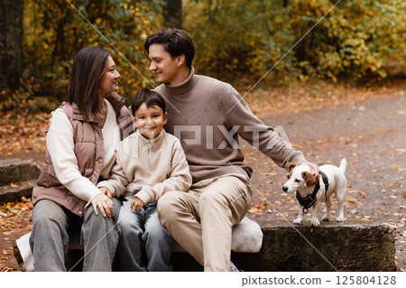 Happy family of three with dog sitting on bench in autumn park 125804128