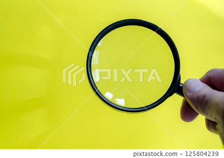 Hand holding a magnifying glass against a bright yellow background. Searching, examining, focusing or investigation concept. 125804239