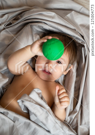 Top view of cute caucasian toddler playing ball in bed. Top view of cute caucasian toddler playing ball in bed. 125804773
