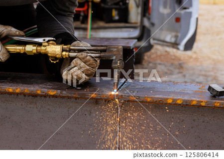 Welder is performing metal cutting with a torch, creating sparks at construction site under works day 125806414