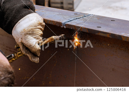 Worker uses welding torch to cutting metal pieces in workshop environment, sparks flying around. Worker uses welding torch to cutting metal pieces in workshop environment, sparks flying around. 125806416