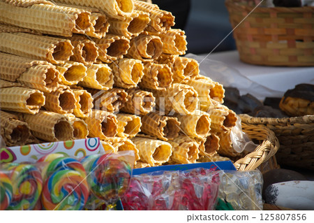 Delightful pile of golden wafer rolls with colorful lollipops and sweets from the market stall. 125807856