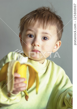 Little child with brown eyes eating a banana 125808087
