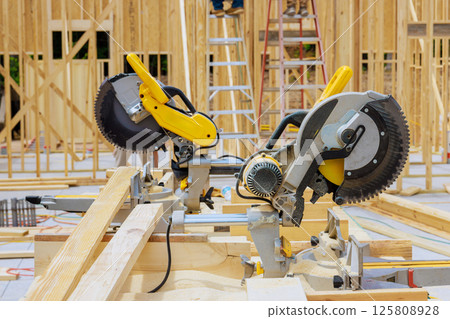 Workers use miter saws to cut wood at construction site with wooden framework in progress under works day 125808928