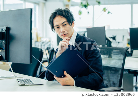 一位男老闆坐在辦公室的辦公桌前使用電腦 125808966