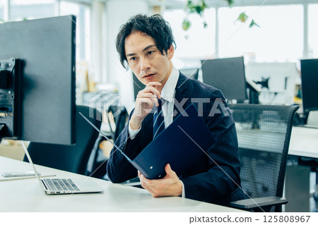 A male boss sitting at a desk in an office and using a computer 125808967
