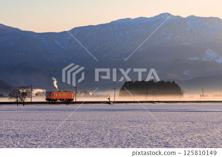 越後南線上的一輛單車柴油列車穿過積雪覆蓋的鐵路道口附近的稻田。 125810149