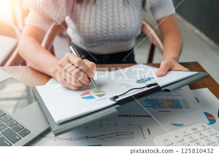 Professional woman reviewing financial documents with charts and graphs, highlighting business analysis and strategy. Professional woman reviewing financial documents with charts and graphs, highlighting business analysis and strategy. 125810432
