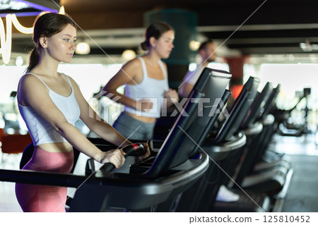 Girl in gym runs with help of treadmill 125810452