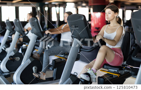 Young woman exercising on exercise bike in gym Young woman exercising on exercise bike in gym 125810473