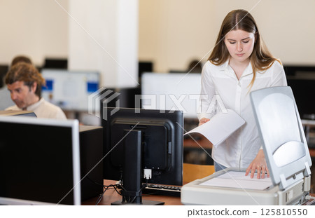 Girl puts paper document into copier, makes copy using office appliances Girl puts paper document into copier, makes copy using office appliances 125810550