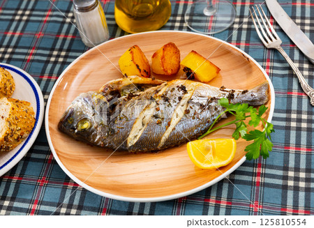 Grilled dorada with baked potatoes, lemon and parsley Grilled dorada with baked potatoes, lemon and parsley 125810554