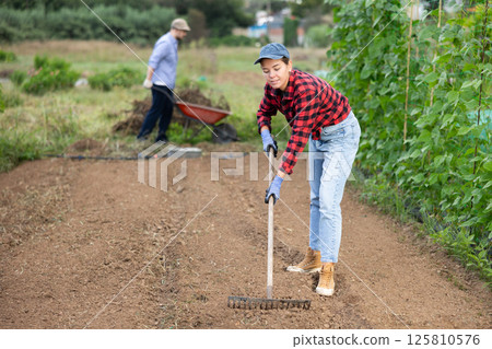 Girl working in garden, raking soil on patch while preparing for planting seedlings Girl working in garden, raking soil on patch while preparing for planting seedlings 125810576