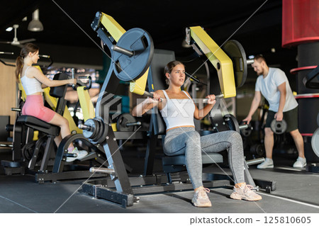 Athletic woman work out muscles of arms and hands on simulator in fitness club Athletic woman work out muscles of arms and hands on simulator in fitness club 125810605