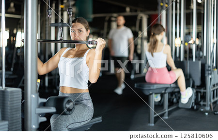 Slender athletic woman work out muscles of hands on cable crossover machine in fitness club 125810606