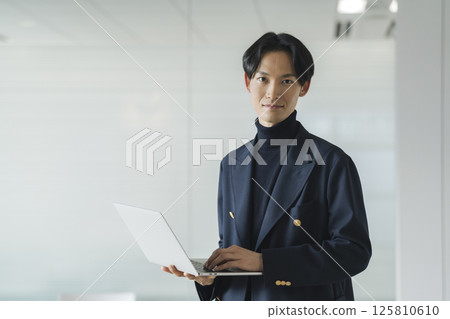 A businessman in his 30s holding a laptop computer, looking at the camera A businessman in his 30s holding a laptop computer, looking at the camera 125810610