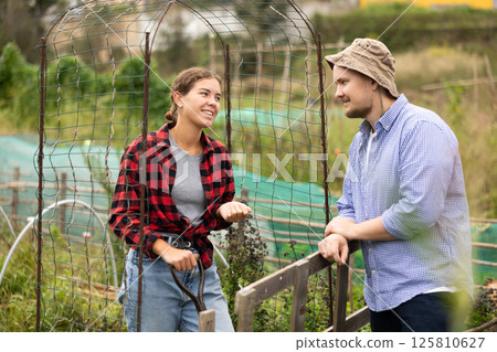 Cheerful female farmer friendly talking to her male neighbour on backyard Cheerful female farmer friendly talking to her male neighbour on backyard 125810627