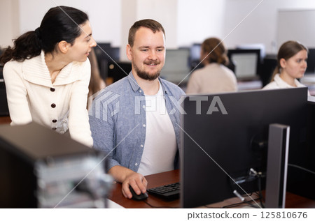 Female teacher helps man with learning on computer in university computer lab 125810676