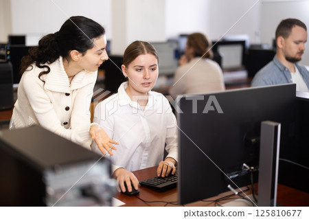 Young female teacher helps woman work on computer 125810677