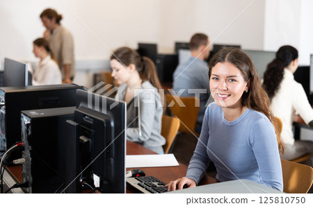 Young woman student of computer courses looks at monitor screen, types on keyboard and does work Young woman student of computer courses looks at monitor screen, types on keyboard and does work 125810750