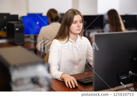 Young woman student of computer courses looks at monitor screen, types on keyboard and does work 125810753