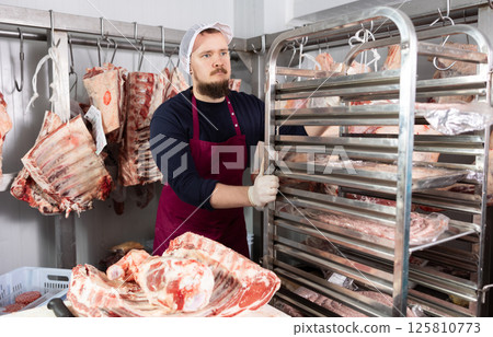 Butcher shop worker organizing meat racks in cold storage Butcher shop worker organizing meat racks in cold storage 125810773